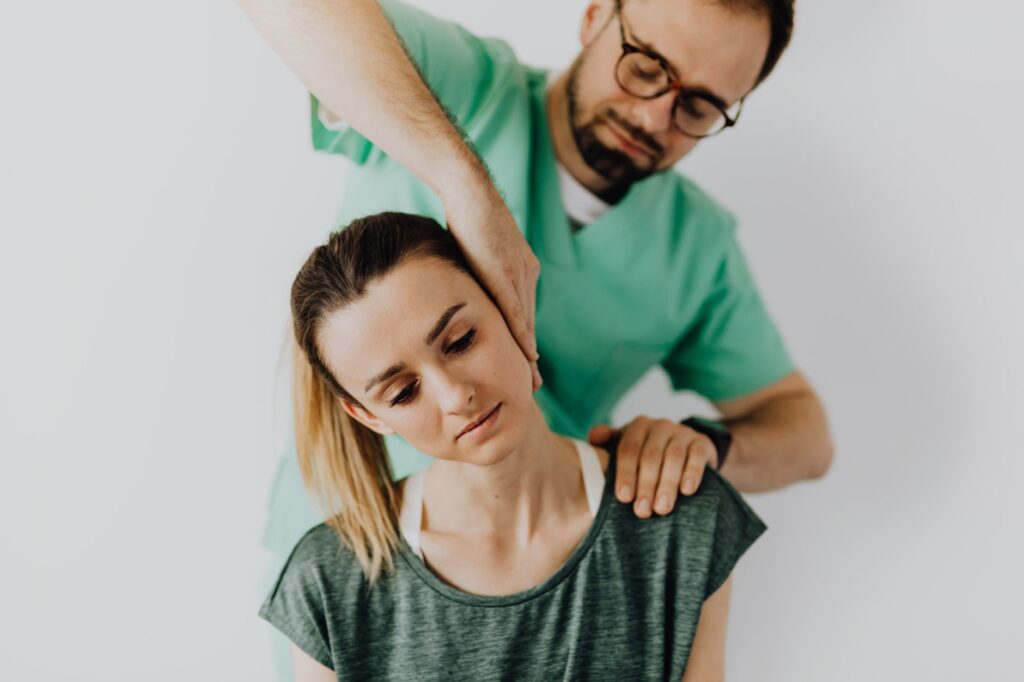 Concentrated doctor massage therapist in medical uniform doing therapeutic neck massage for calm young female patient in